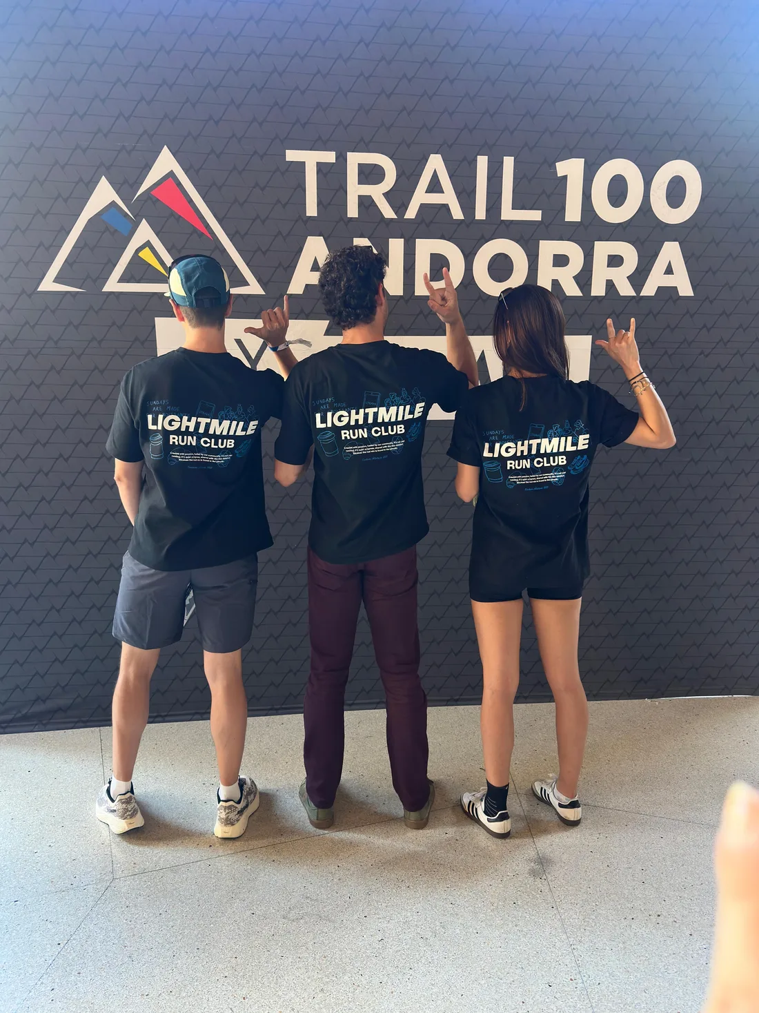 Three Lightmile runners seen from behind in front of the Trail 100 Andorra wall